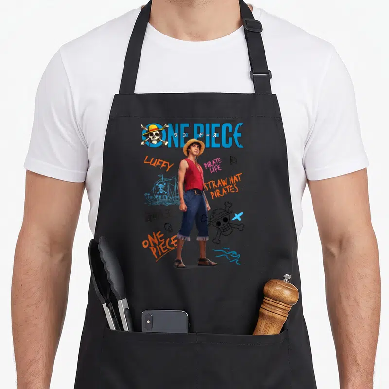 Tablier de cuisine noir avec Luffy Pirate Life, Straw Hat Pirates et logos One Piece en couleurs vives sur fond sombre.