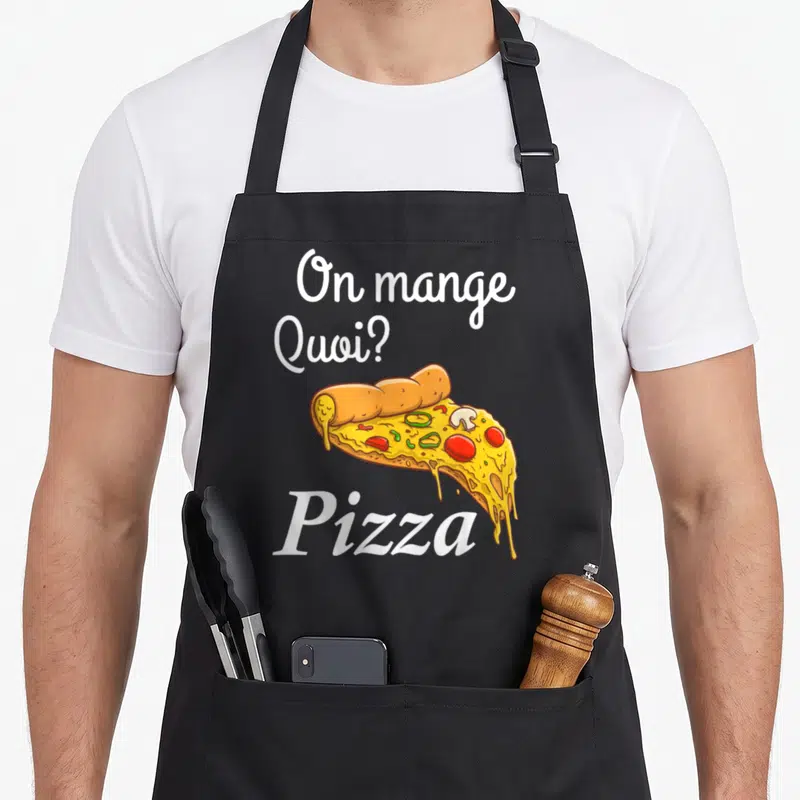 Tablier de cuisine noir avec l'inscription On mange Quoi ? Pizza et une illustration colorée d'une tranche de pizza garnie.