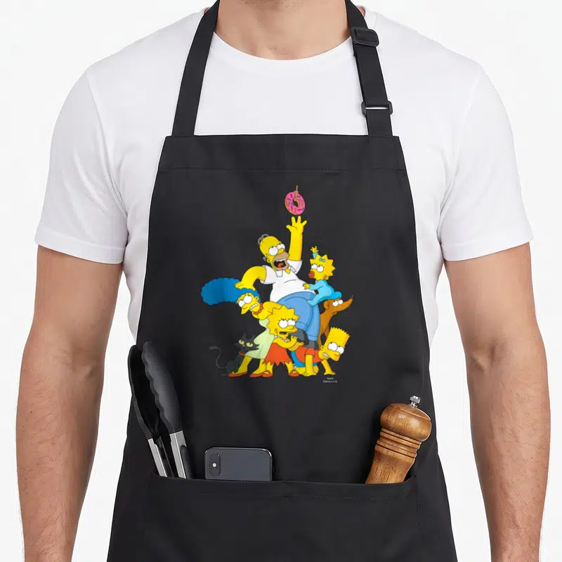 Tablier de cuisine noir avec illustration colorée de la famille Simpson s'étirant vers un donut suspendu en l'air.