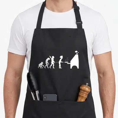 Tablier de cuisine noir avec une illustration blanche représentant l'évolution humaine se terminant par un pizzaiolo insérant une pizza dans un four à bois.