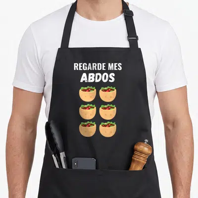 Tablier de cuisine noir avec texte Regarde mes abdos et six illustrations de tacos disposés en grille.