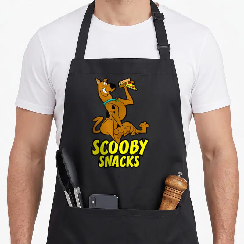 Tablier de cuisine noir avec un chien tenant une pizza et le texte Scooby Snacks en jaune.