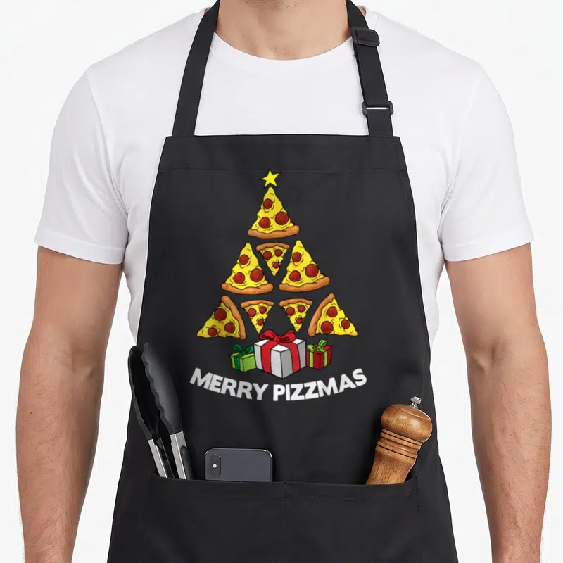 Tablier de cuisine noir avec un arbre de Noël composé de tranches de pizza et des cadeaux en dessous.