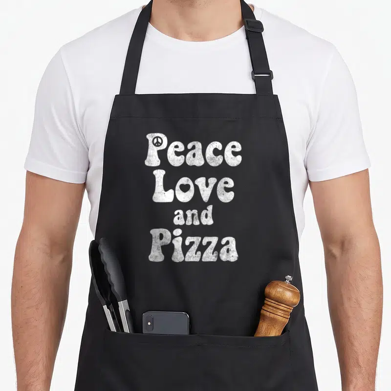 Tablier de cuisine noir avec inscription blanche Peace Love and Pizza et symboles gravés sur les lettres.