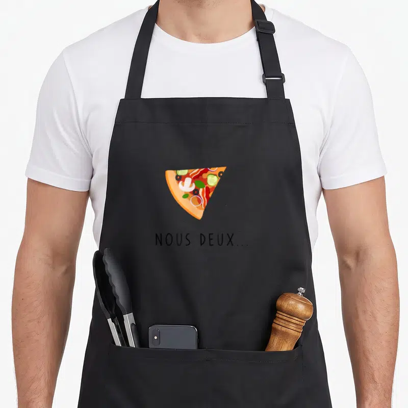 Tablier de cuisine noir avec une illustration de part de pizza et le texte Nous deux imprimé en dessous.