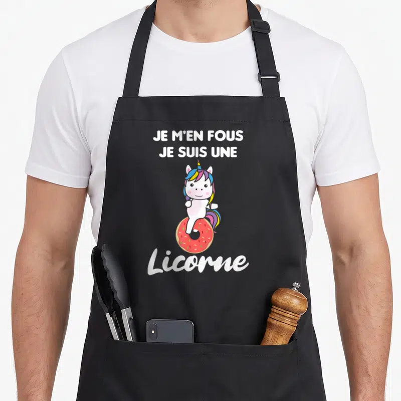 Tablier de cuisine noir avec une licorne blanche assise sur un donut rose et le texte Je m'en fous je suis une licorne en blanc.
