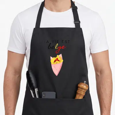 Tablier de cuisine noir avec une illustration de frites belges au ketchup et le texte La vie est belge en typographie mixte.