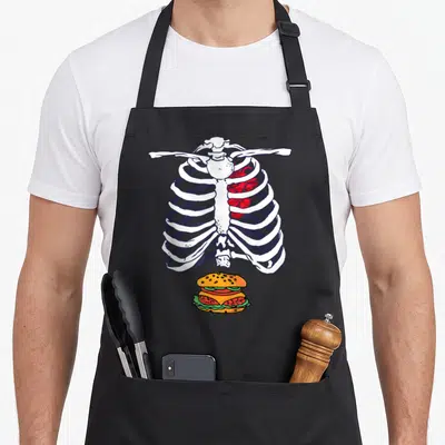 Tablier de cuisine noir avec illustration squelette torse et hamburger coloré au centre.