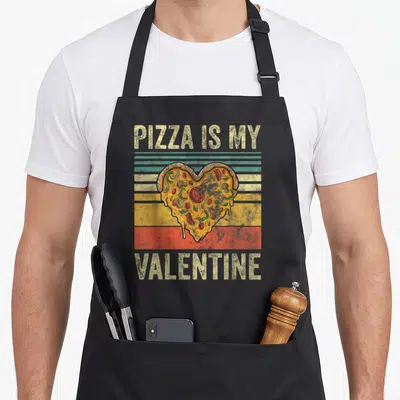 Tablier de cuisine noir avec une part de pizza en forme de cœur et texte vintage.
