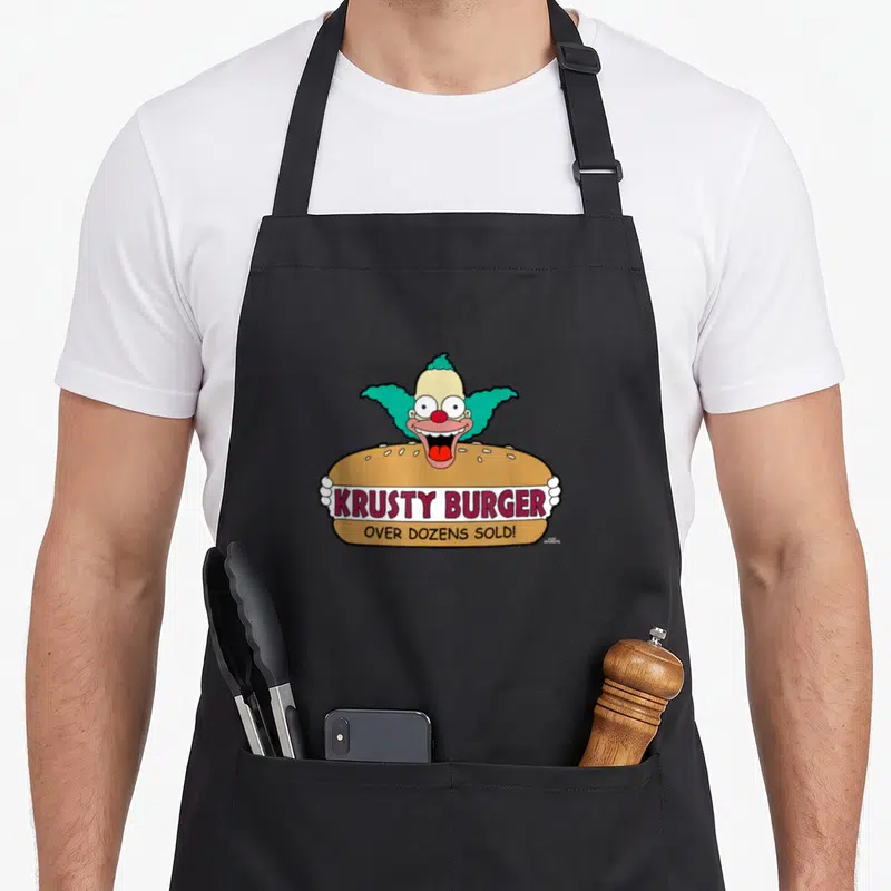 Tablier de cuisine noir avec Krusty Burger et le clown aux cheveux verts émergeant d'un hamburger coloré.