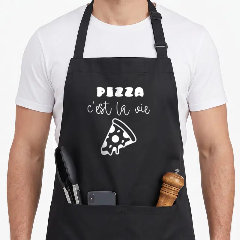 Tablier de cuisine noir avec une tranche de pizza blanche et le texte Pizza c'est la vie imprimé au centre.
