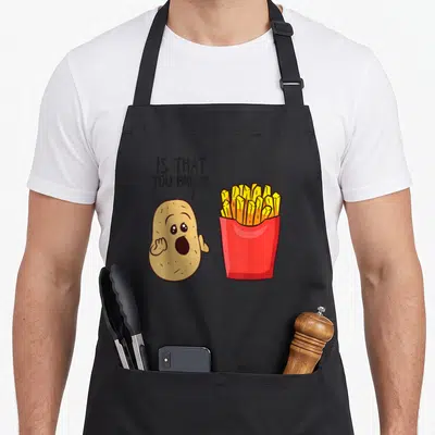 Tablier de cuisine noir avec une patate surprise pointant vers un paquet de frites jaunes dans un emballage rouge.
