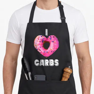Tablier de cuisine noir avec un donut rose en forme de cœur et l'inscription CARBS en lettres blanches stylisées.