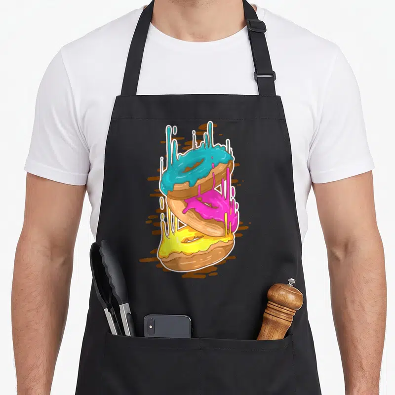 Tablier de cuisine noir avec illustration de trois beignets aux glaçages bleu rose et jaune qui tombent