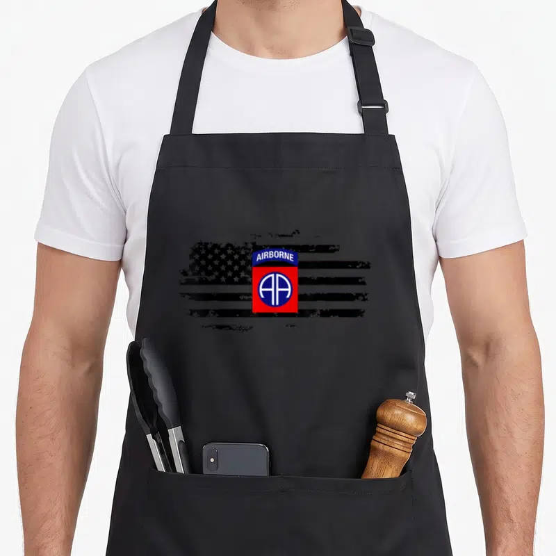 Tablier de cuisine noir avec logo Airborne rouge et drapeau stylisé en noir et blanc.