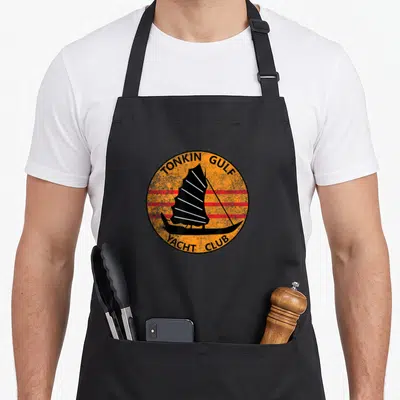 Tablier de cuisine noir avec logo circulaire orange montrant un voilier à voile latine et l'inscription Tonkin Gulf Yacht Club.