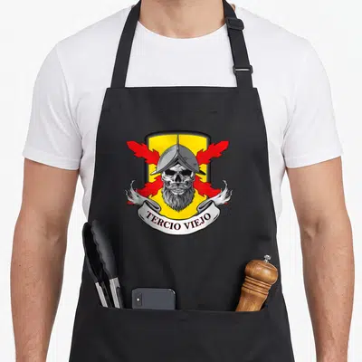 Tablier de cuisine noir avec un emblème de crâne de soldat barbu, casque, ailes rouges et inscription Tercio Viejo sur ruban blanc.