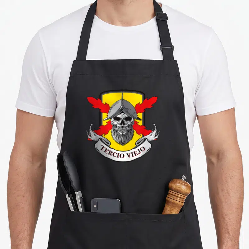 Tablier de cuisine noir avec un emblème de crâne de soldat barbu, casque, ailes rouges et inscription Tercio Viejo sur ruban blanc.