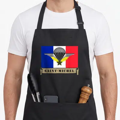 Tablier de cuisine noir avec le logo Saint-Michel parachutiste sur fond tricolore français et une banderole beige en bas.