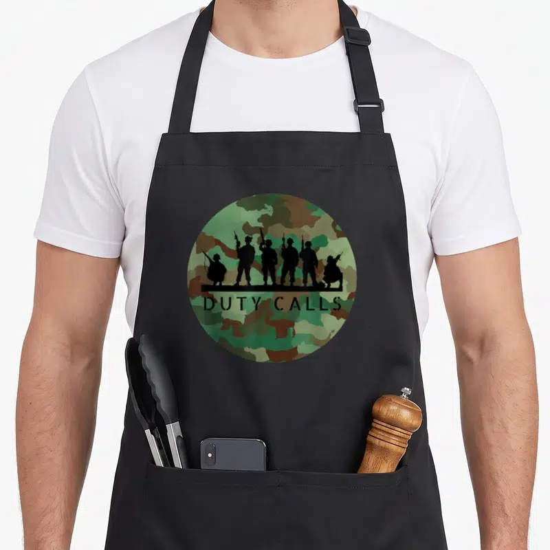 Tablier de cuisine noir avec six silhouettes de soldats sur fond camouflage vert et brun portant l'inscription Duty Calls Cool Camouflage.