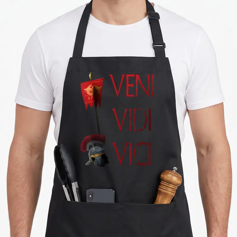 Tablier de cuisine noir avec illustration d'un casque romain, d'une bannière rouge et du texte Veni Vidi Vici en lettres rouges.