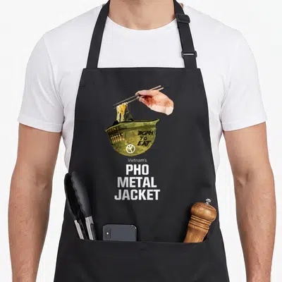 Tablier de cuisine noir avec illustration d'un casque militaire transformé en bol de pho et une main tenant des baguettes.