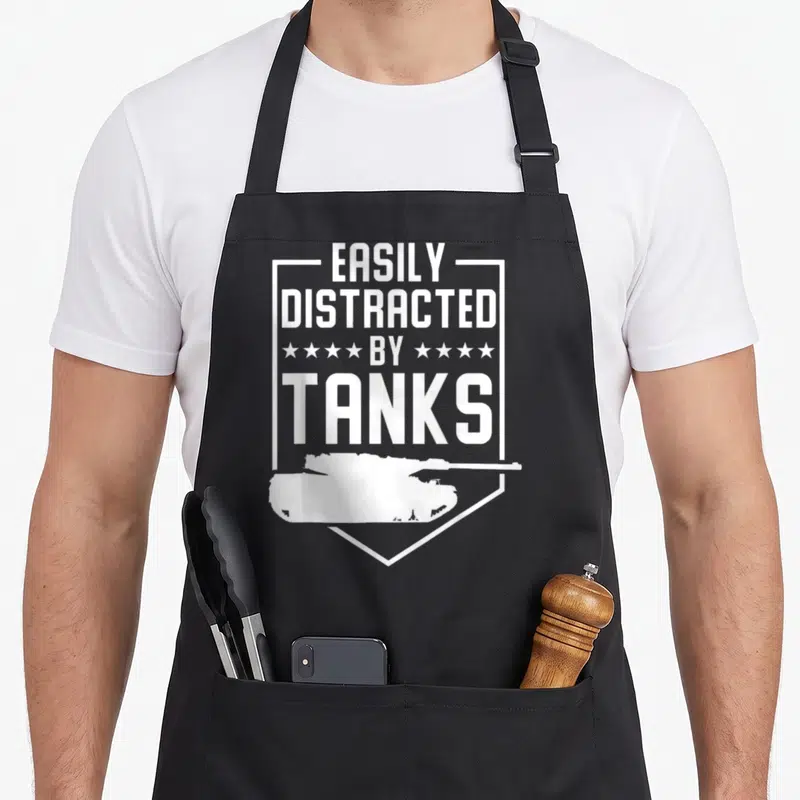 Tablier de cuisine noir avec inscription EASILY DISTRACTED BY TANKS et silhouette de char blindé en blanc.