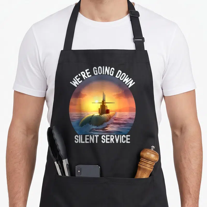 Tablier de cuisine noir avec illustration circulaire d'un sous-marin au coucher du soleil et texte blanc We're Going Down Silent Service.