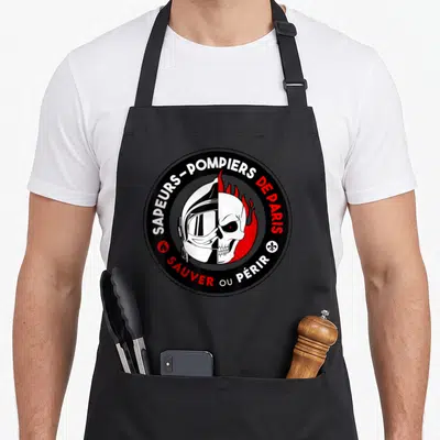 Tablier de cuisine noir avec un logo circulaire Sapeurs-Pompiers de Paris montrant un casque et une tête de mort.