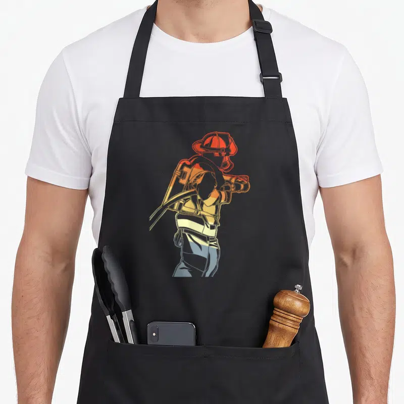 Tablier de cuisine noir avec illustration stylisée d'un pompier portant un tuyau en dégradé orange et bleu.
