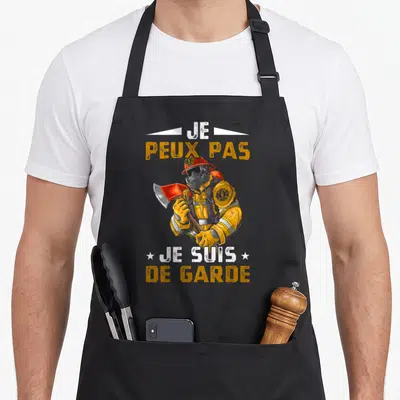 Tablier de cuisine noir avec illustration d'un pompier en tenue jaune tenant une hache et le texte Je peux pas je suis de garde.