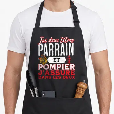 Tablier de cuisine noir avec inscription parrain pompier et illustration d'un sapeur-pompier tenant une hache.