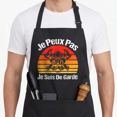 Tablier de cuisine noir avec illustration casque viking et texte blanc Je Peux Pas Je Suis De Garde sur fond orange.