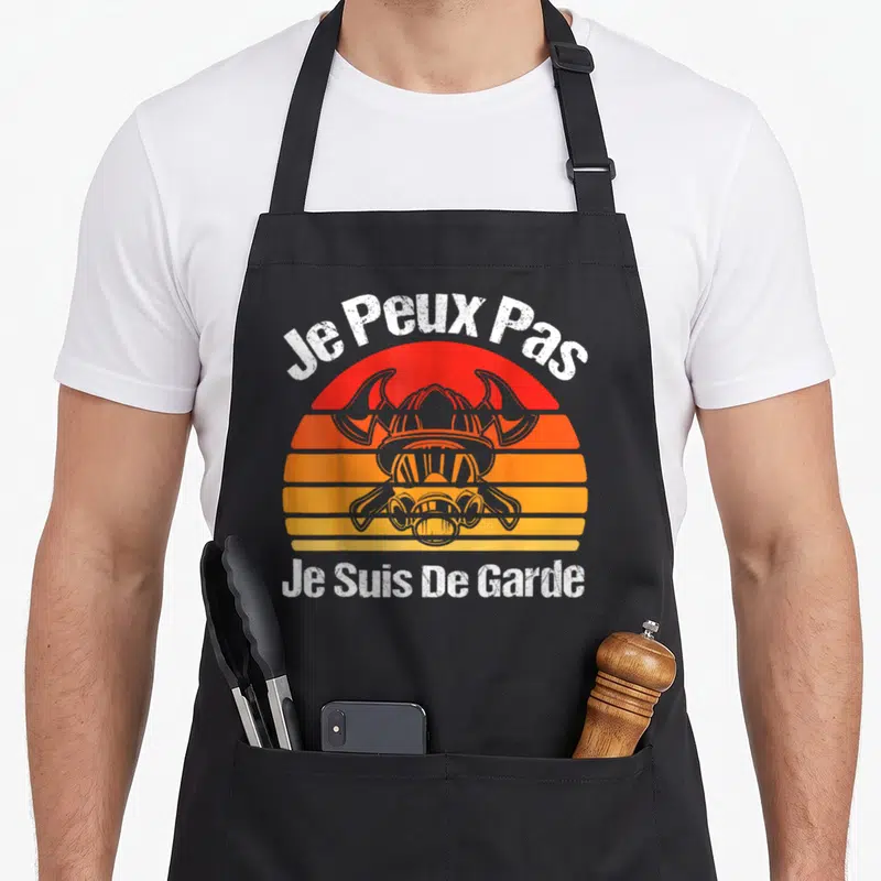 Tablier de cuisine noir avec illustration casque viking et texte blanc Je Peux Pas Je Suis De Garde sur fond orange.