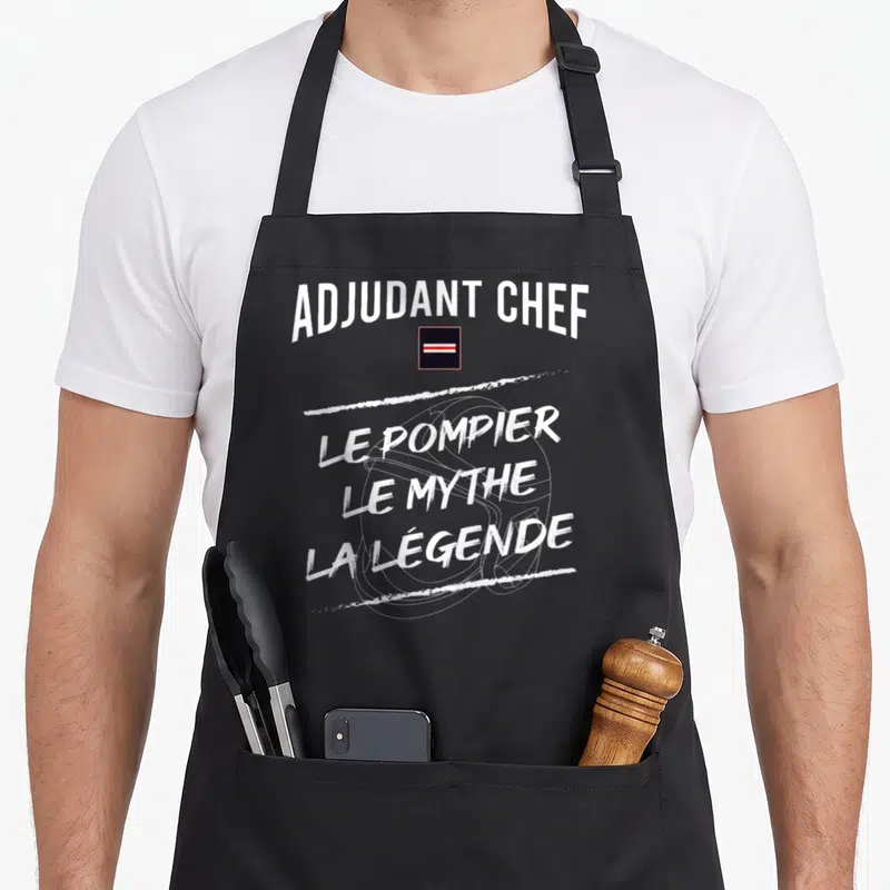 Tablier de cuisine noir avec linscription Adjudant Chef Le Pompier Le Mythe La Légende en blanc et un insigne rectangulaire.
