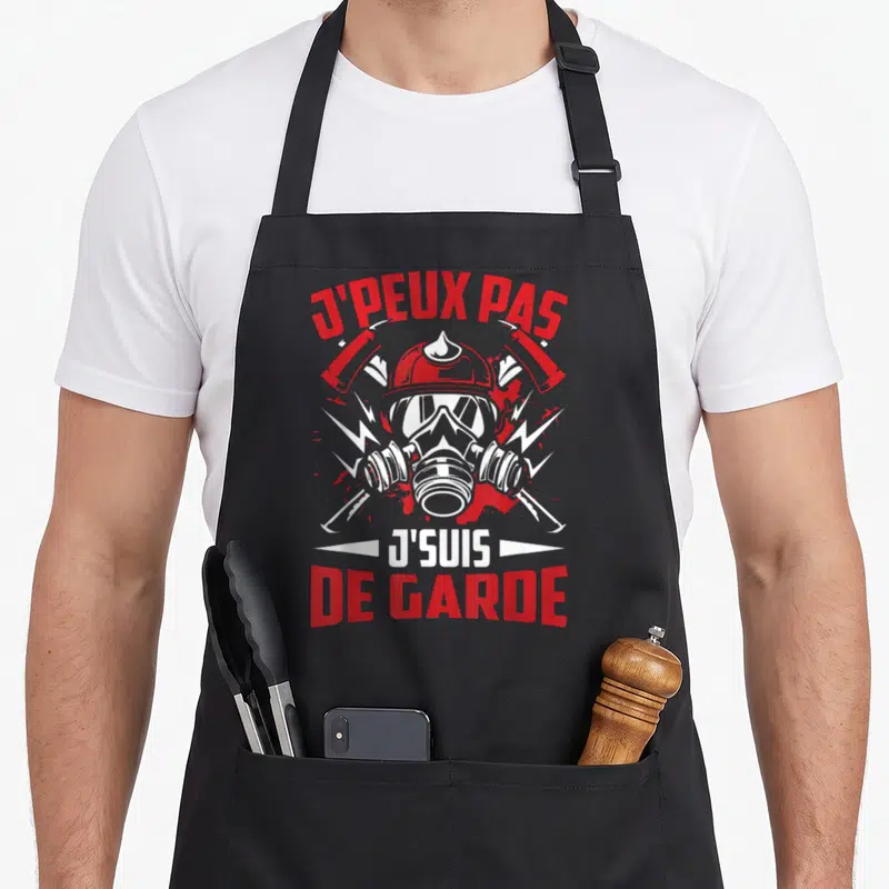 Tablier de cuisine noir avec illustration casque pompier et texte J'peux pas j'suis de garde en rouge et blanc.