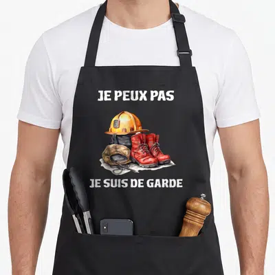Tablier de cuisine noir avec casque orange, bottes rouges et texte Je peux pas je suis de garde imprimé en blanc.