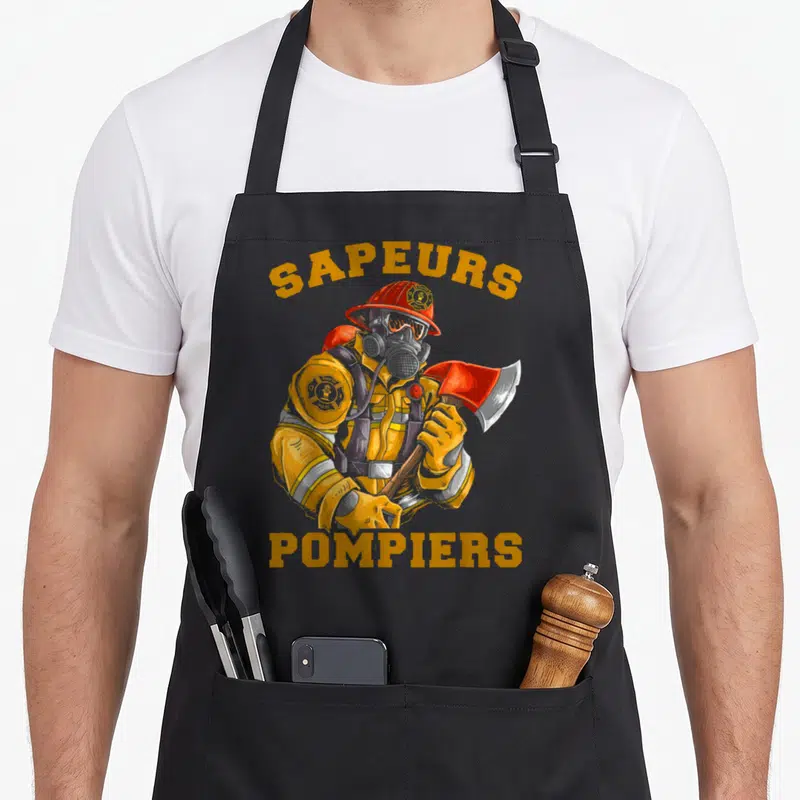 Tablier de cuisine noir avec illustration d'un sapeur-pompier portant casque rouge, masque à gaz et tenant une hache.
