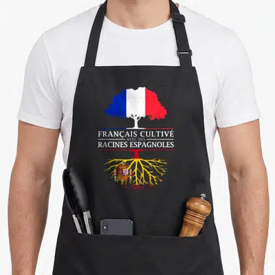 Tablier de cuisine noir avec un arbre aux couleurs du drapeau français et le texte Français cultivé avec des racines espagnoles sur fond gris.