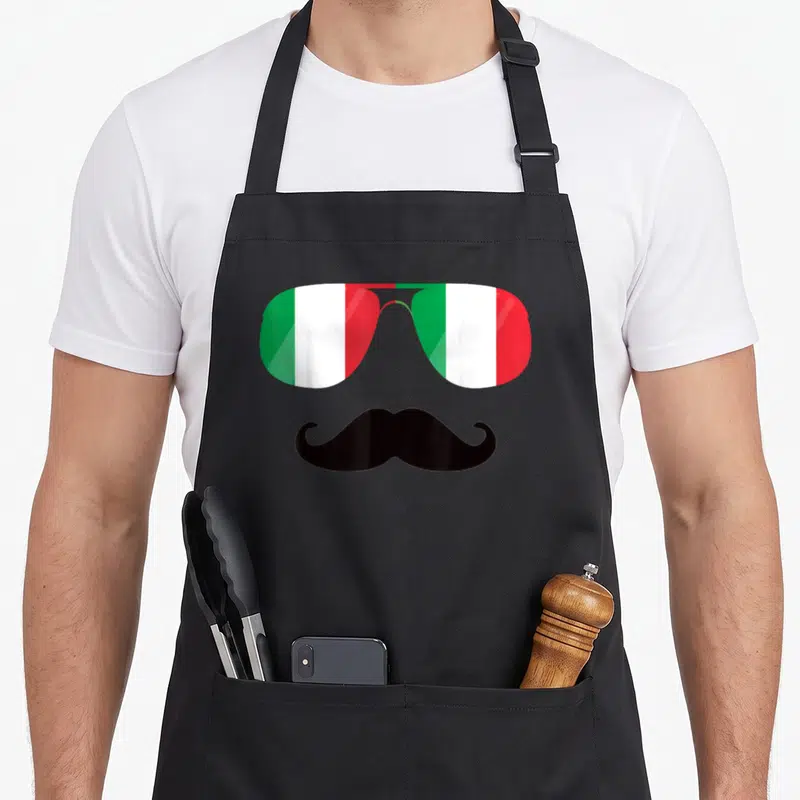 Tablier de cuisine noir avec lunettes aux verres tricolores verts blancs rouges et moustache noire courbée sous les verres.