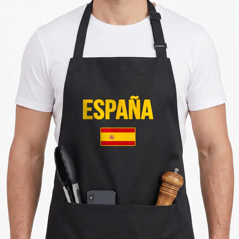 Tablier de cuisine noir avec le mot España en jaune et un drapeau espagnol rectangulaire centré en dessous.