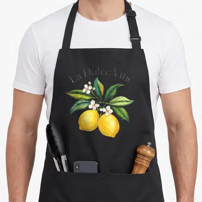 Tablier de cuisine noir avec deux citrons jaunes, feuilles vertes et fleurs blanches sous l'inscription La Dolce Vita.