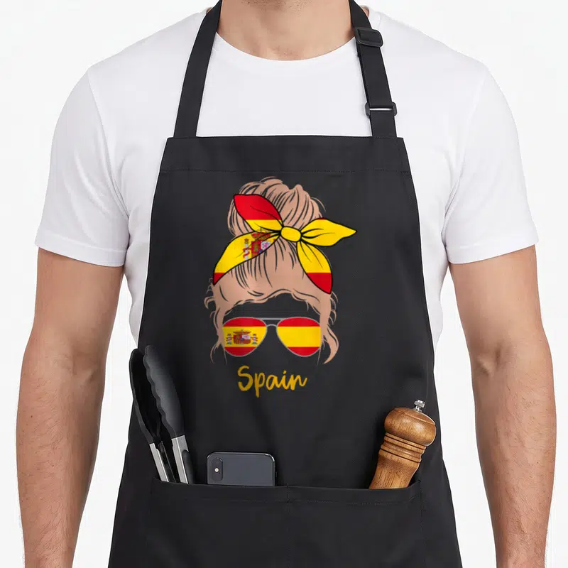Tablier de cuisine noir avec illustration d'une femme blonde au nœud et lunettes aux couleurs espagnoles
