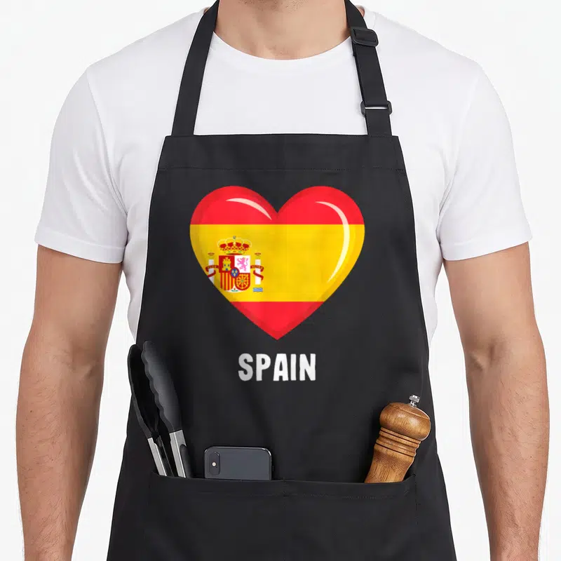 Tablier de cuisine noir avec un grand cœur rouge et jaune portant le drapeau espagnol et l'inscription SPAIN en bas.