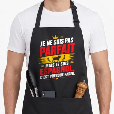 Tablier de cuisine noir avec l'inscription Je ne suis pas parfait mais je suis Espagnol surmonté d'une couronne et d'un taureau gris.