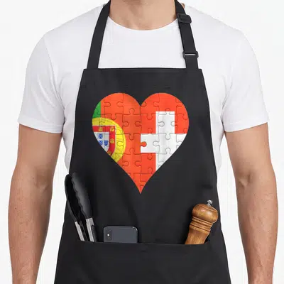 Tablier de cuisine noir avec un grand cœur formé par les drapeaux du Portugal et de la Suisse en motif puzzle.