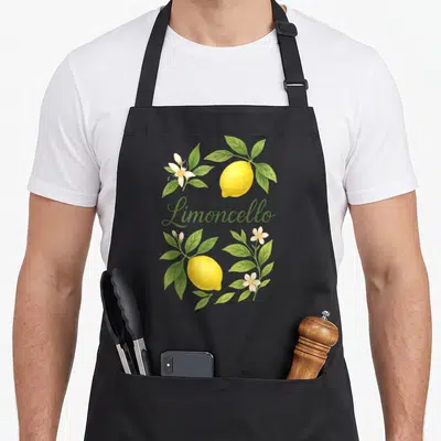 Tablier de cuisine noir avec deux citrons jaunes, des feuilles vertes, des fleurs blanches et le mot Limoncello en écriture cursive verte.
