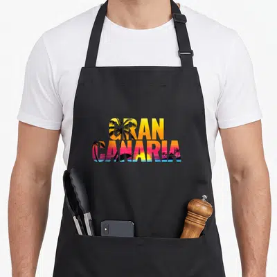 Tablier de cuisine noir avec l'inscription Gran Canaria remplie de palmiers et dun coucher de soleil multicolore.
