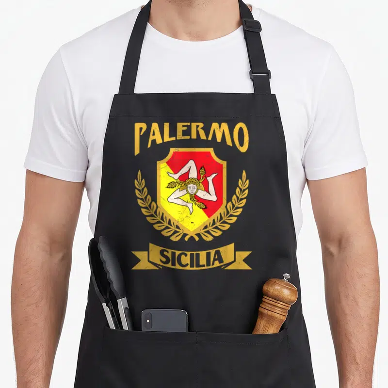 Tablier de cuisine noir avec le blason de Palerme, l'inscription Sicilia et une triskèle dorée sur fond rouge et jaune.