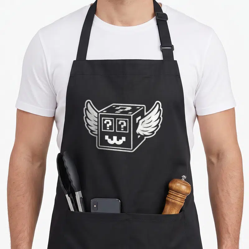 Tablier de cuisine noir avec un cube pixelisé blanc aux ailes et deux points d'interrogation sur le visage.